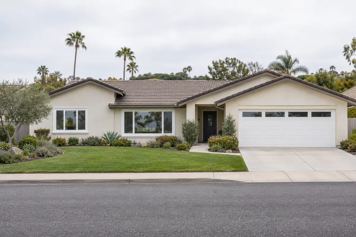 Single-story cream stucco ranch home with new white vinyl windows, a green lawn and low landscaping under an overcast sky