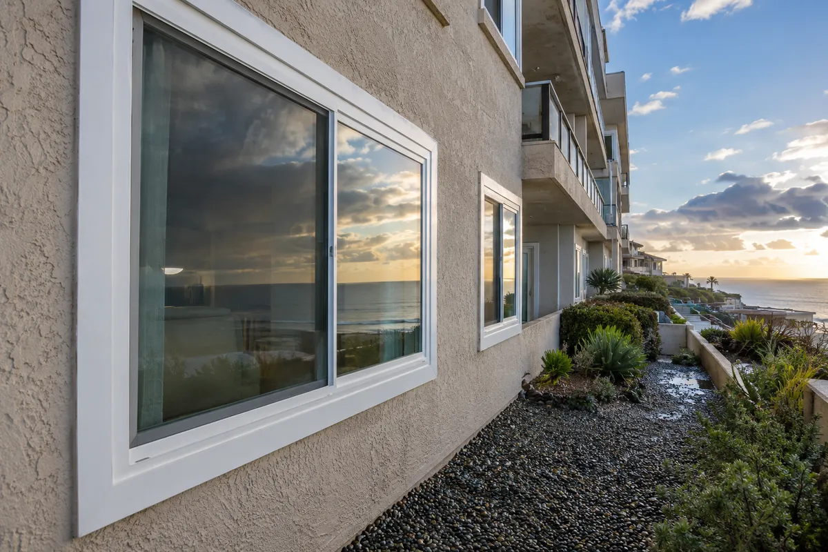 Close view of a white-framed sliding window on a bluff-top condominium building with the ocean reflected in the glass
